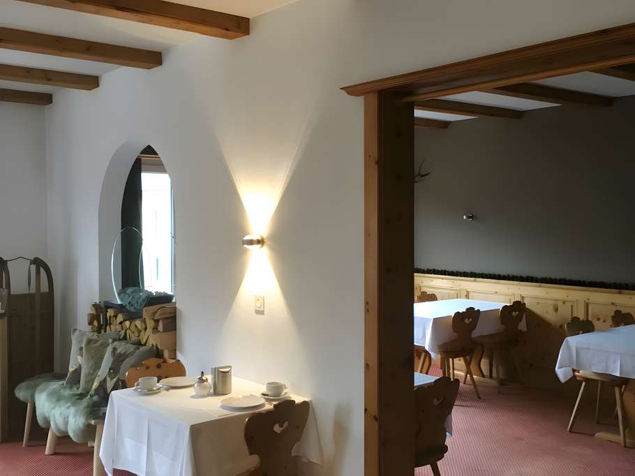 Einladender, alpenländischer Speiseraum, der durch warme Wandbeleuchtung, rustikale Deckenbalken und traditionelle Holzmöbel eine gemütliche Stimmung vermittelt.
